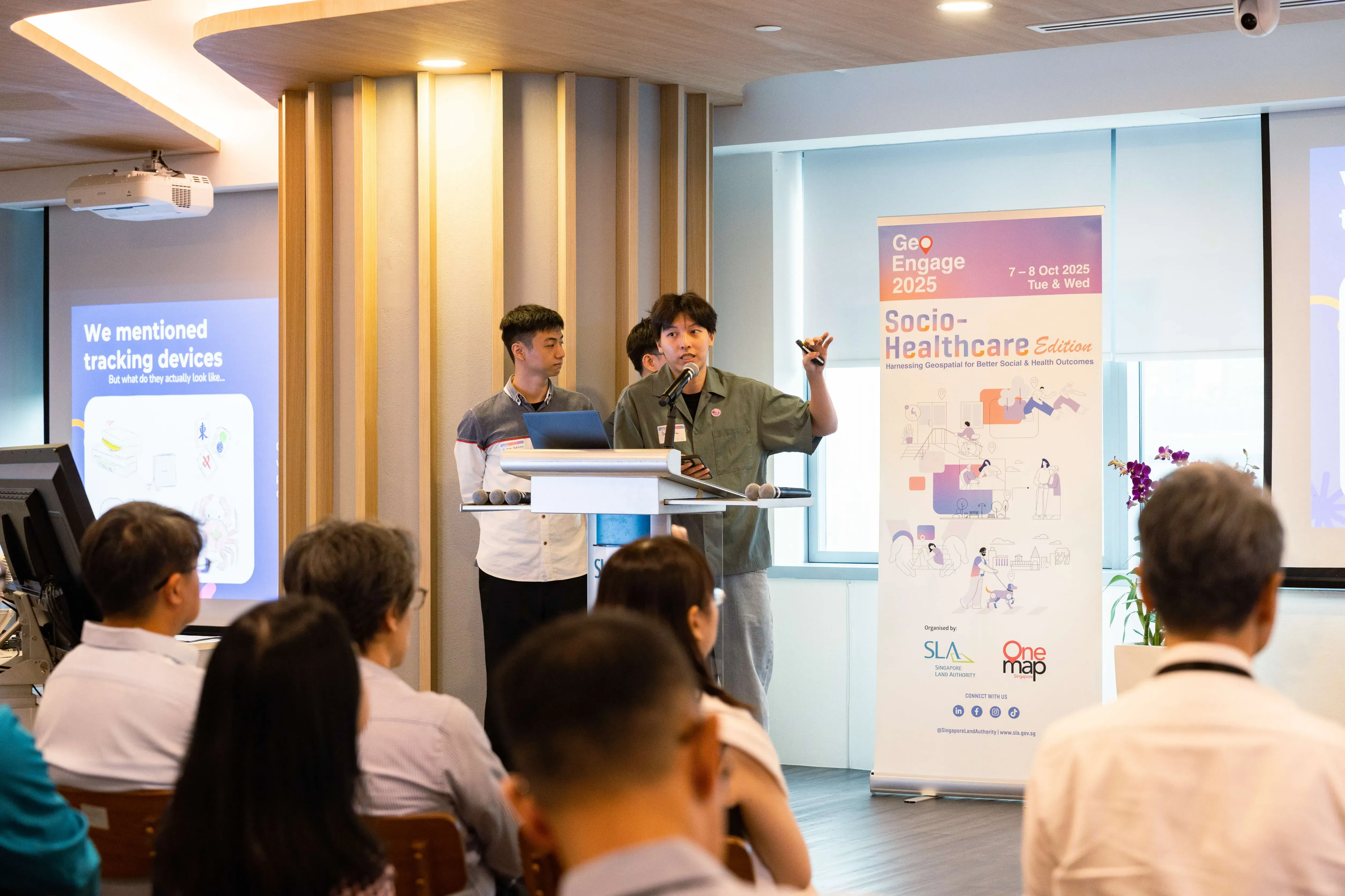 Team 1 from NTU speaks at a podium during GeoEngage 2025 Socio-Healthcare Edition event, with an audience seated in front.